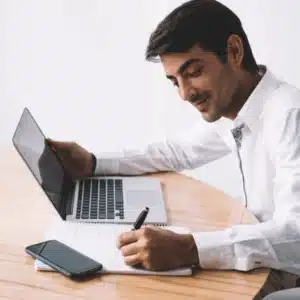 Man writes notes while using a laptop, highlighting cloud computing advantages in modern remote work