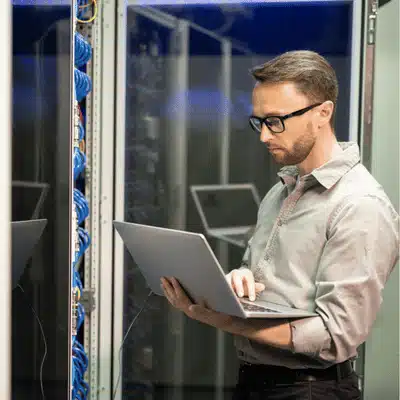 Photo shows engineer using laptop beside data cabinets, highlighting it support company monitoring services onsite