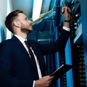 IT manager inspects rack equipment with clipboard, reviewing server backup strategy, security settings, and performance