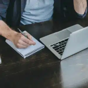 Administrator drafts recovery checklist beside laptop, documenting schedules, contacts, and backup verification procedures for continuity