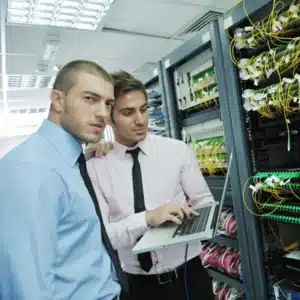 IT specialists analyze switch connections and configuration on laptop beside cabling; image shows network operations