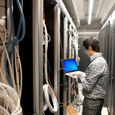 Photo of technician checking server racks with laptop, illustrating it support company network maintenance work