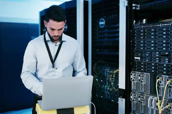 Technician checks rack servers using laptop, monitoring uptime; IT services for small business support operations
