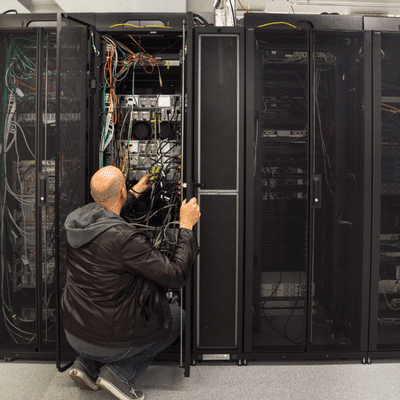 Engineer kneels inside server room, tracing cables and hardware connections; Lenovo vs Dell servers today
