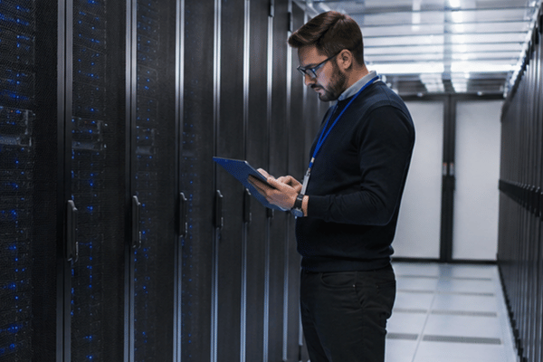 An IT professional reviews server racks with a tablet in a modern data center, representing how top server companies support secure workload planning
